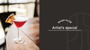 Artist’s Special cocktail with a vivid ruby-red color in a martini glass, garnished with a pineapple wedge on a wooden bar table