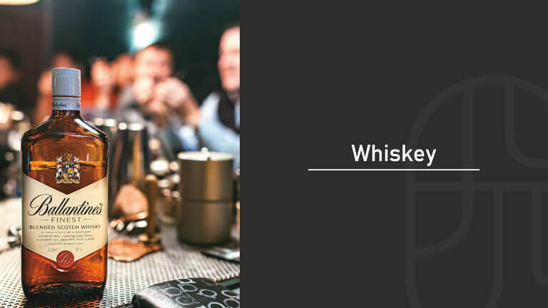 Bottle of Ballantine’s Finest blended Scotch whisky on a bar counter, with a lively blurred bar scene in the background and the title “Whiskey”