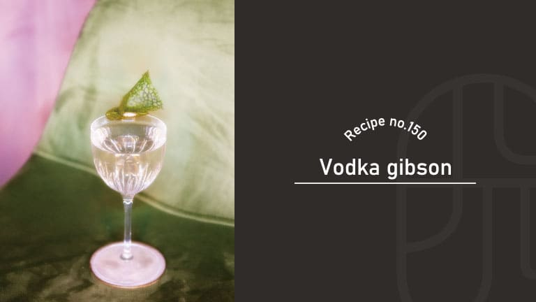 Vodka Gibson cocktail in an etched stemmed glass, a crystal-clear drink with a delicate green leaf garnish, set on a green velvet surface with a soft pink backdrop — Recipe no.150