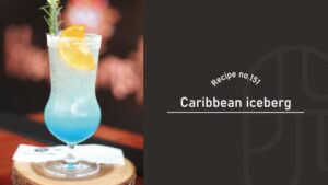 Caribbean Iceberg cocktail in a hurricane glass with a sugar rim, an icy drink fading from clear to bright blue at the bottom, garnished with an orange slice and a rosemary sprig on a wooden coaster — Recipe no.151