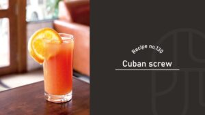 Cuban Screw cocktail with a bright orange color in a tall glass, garnished with an orange slice on a wooden table in a cozy café