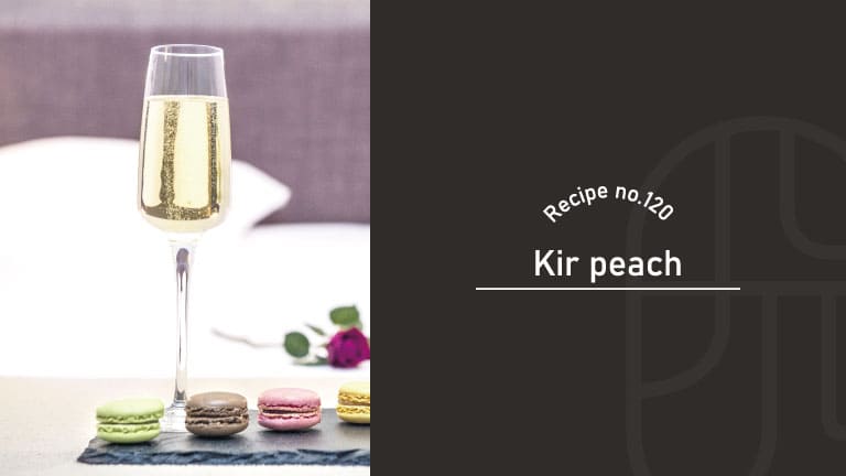 Kir Peach cocktail in a tall champagne flute with a pale golden color, served with colorful macarons on a slate board and a rose in the background