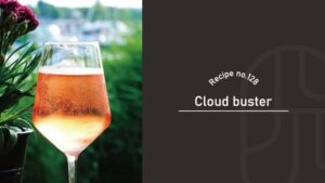 Cloud Buster cocktail with fine rising bubbles in a wine glass, glowing a soft peach color outdoors beside pink carnations and lush greenery