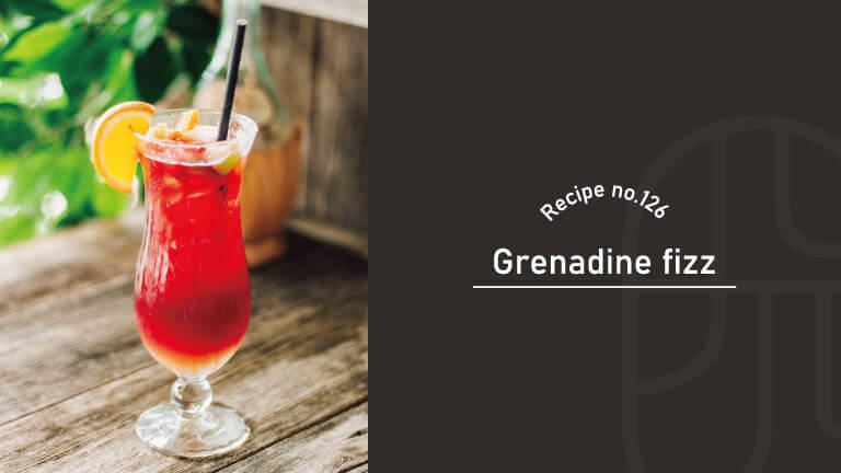 Grenadine Fizz cocktail with a vivid ruby-red color in a hurricane glass, garnished with an orange slice and a black straw on a rustic wooden table outdoors