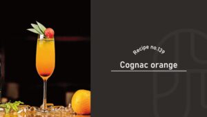 Cognac Orange cocktail in a tall flute glass, glowing orange with a red layer at the bottom and garnished with a cherry and leaves, beside a fresh orange — Recipe no.139