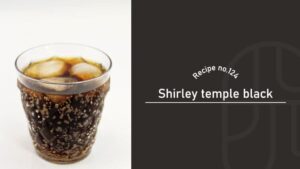 Shirley Temple Black, a dark cola-colored mocktail with ice and lively bubbles, in a faceted glass on a white background