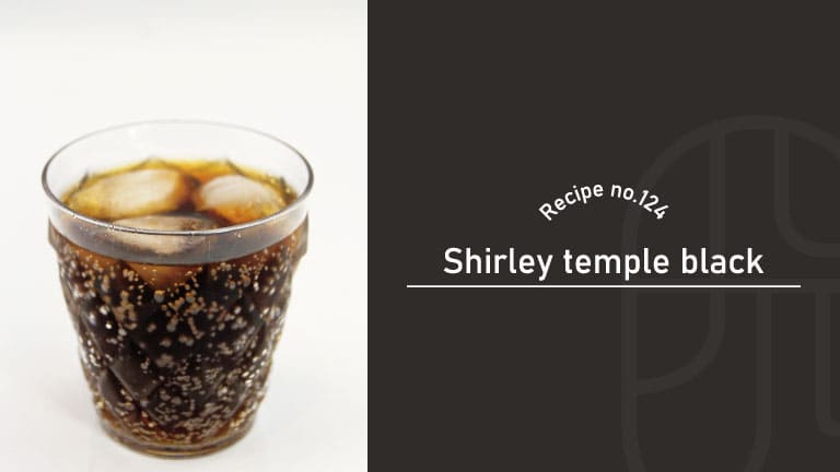Shirley Temple Black, a dark cola-colored mocktail with ice and lively bubbles, in a faceted glass on a white background