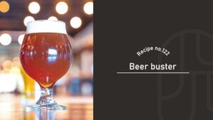 Beer Buster cocktail with an amber-red color and a thick white head in a tulip beer glass on a bar counter with warm bokeh lights