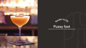 Pussyfoot mocktail with a frothy golden-orange color in a coupe glass, garnished with a passion fruit slice on a bar counter with warm lights